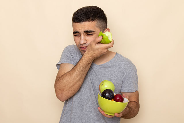 a young man with tooth pain while biting a fruit seeking an emergency dentist near me
