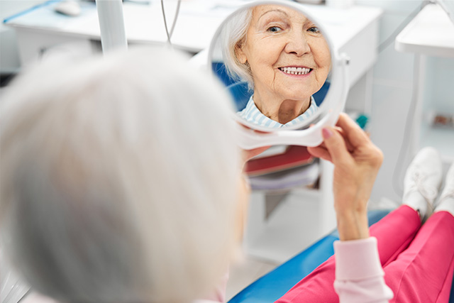 a patient looking at herself in mirror after getting dental implants from a dentist in modesto ca